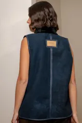 Chaleco de cuero azul con acabado gamuzado, cuello alto con forro de piel sintética negra, cierre frontal con botones tipo toggle y bolsillos laterales amplios.