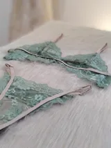 Conjunto de lencería compuesto por un bralette triangular y una bombacha tipo tanga, confeccionados en encaje color verde oliva con detalles y elásticos en tono tostado.