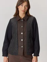 Campera de diseño híbrido con paneles frontales acolchados en color negro, solapa central y cuello en lana marrón con textura de espiga, y mangas de lana negra. Presenta cierre frontal con botones y forro interior de lana.