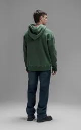 Hoodie oversize color verde, confeccionado en frisa premium con textura gamuzada. Presenta capucha ajustable con cordones personalizados, bolsillo frontal tipo canguro y puños con abertura para pulgar.