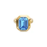 Anillo de aleación de metales con baño de oro 18k, presenta un diseño minimalista con un cristal azul facetado de corte rectangular en el centro.