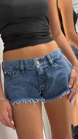 Short de jean de tiro bajo con diseño de cinco bolsillos, cierre frontal con botón metálico y terminaciones deshilachadas en el ruedo.