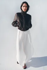 Chaqueta tipo bomber de piel con cuello alto, manga larga con hombreras y puños elásticos. Presenta bolsillos delanteros, bajo elástico y cierre frontal con cremallera y botones ocultos por solapa.