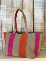 Cartera de cuero tipo shopper de diseño amplio, con tiras verticales en colores marrón, naranja y fucsia. Cuenta con doble asa de hombro y cierre superior.
