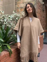 Ruana de tejido de lana merino color tostado, con diseño abierto, mangas cortas y detalle de flecos en el ruedo.
