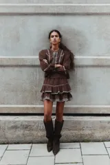 Blusa de algodón con textura arrugada, color marrón, con detalles bordados en contraste en el frente y las mangas. Presenta escote redondo, cierre frontal con botones, mangas globo largas y puños abotonados.