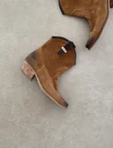 Bota corta estilo western de cuero color marrón, con taco cuadrado de 5 cm y diseño clásico. Presenta un acabado desgastado en la puntera y el talón.