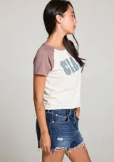 Remera blanca con mangas cortas color marrón y estampado frontal con la palabra "CIAO" en celeste con estrellas rosadas.