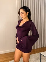 Vestido corto de color morado, confeccionado en tela suave y elastizada con caída. Cuenta con escote drapeado, mangas largas acampanadas y un diseño ajustado que acompaña la silueta.