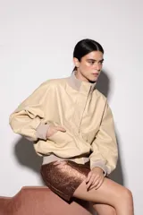 Chaqueta de cuero estilo bomber, con cuello alto, puños y cintura de tejido de punto acanalado. Presenta cierre frontal con cremallera y dos bolsillos laterales con solapa.