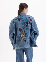 Chaqueta de denim de corte oversize con diseño de bordados y estampas exclusivas. Posee cuello clásico, cierre frontal con botones metálicos y bolsillos con solapa en el pecho.
