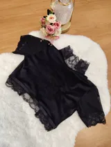 Top de terciopelo negro con cuello alto, detalles de encaje en el cuello y mangas, y paneles de microtul. Presenta espalda descubierta.