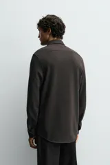 Camisa de corte relajado confeccionada en tejido de algodón con textura. Presenta cuello italiano, manga larga con puños abotonados y cierre frontal mediante botonadura.