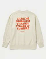 Buzo de cuello redondo en color beige, con diseño de corte holgado y mangas largas. Presenta un pequeño bordado en el pecho con la inscripción 'UNIFORM CLUB' en color naranja y un dobladillo asimétrico con tajo lateral.