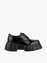 Zapato de estilo oxford o derby con plataforma gruesa y dentada, acabado en charol negro brillante.