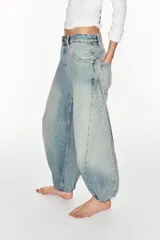 Jeans de mezclilla de tiro medio con diseño amplio tipo balloon, costuras marcadas y bajo con puño elástico. Cuenta con bolsillos delanteros y traseros, y cierre frontal con cremallera y botón metálico.