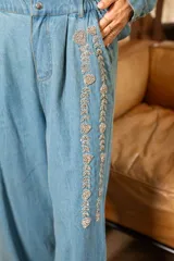 Pantalón de denim celeste con corte amplio y cintura elastizada. Presenta detalles de pedrería en los laterales.
