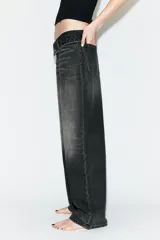 Jeans de mezclilla de tiro medio, corte wide leg y diseño relaxed. Presenta detalles rotos y desgastados en las piernas, y una cinturilla doblada superpuesta con trabillas y cierre frontal con cremallera y botón metálico.