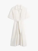 Vestido midi color blanco de Tommy Hilfiger, confeccionado en lino y algodón. Presenta cuello camisero, manga corta, cierre frontal oculto y un cinturón ajustable anudado en la cintura. La falda tiene diseño acampanado y largo por debajo de la rodilla.