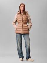 Chaleco puffer acolchado color tostado de la marca Calvin Klein, con diseño sin mangas, cuello alto y capucha desmontable. Cuenta con cierre frontal de cremallera y un cinturón elástico ajustable con hebilla de clip con el logo de la marca.