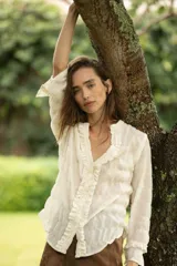 Blusa de manga larga color blanco roto, con cuello en V y volados verticales en el frente.