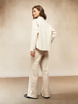 Camisa de manga larga color crudo, con cuello clásico, botones frontales y bolsillo de parche en el pecho. Presenta costuras decorativas en contraste.