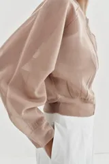 Chaqueta estilo bomber de punto color beige con acabado brillante, cuello redondo, manga larga con puños elásticos y cierre frontal con cremallera.