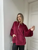 Canguro oversize de plush color bordó, con capucha, mangas globo con puños fruncidos, bolsillo frontal tipo canguro y tajos laterales con tiras ajustables.