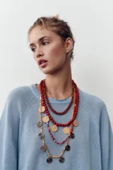 Pack de cinco collares superpuestos con cadenas de diferentes grosores. Incluye collares con cuentas rojas, marrones y amarillas, cuentas de cristal transparentes/rojas, y dijes metálicos circulares con textura martillada dorada y otros con diseño de espiral plateado/negro.