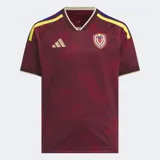Camiseta de fútbol Adidas, modelo Local 2026 para fanáticos, color granate con patrón geométrico de triángulos en tono más oscuro. Presenta cuello en V con ribete beige y detalles en amarillo y azul en los hombros. Lleva el escudo de la selección venezolana y el logo de Adidas bordados.