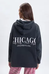 Canguro oversize de color negro con capucha y bolsillo frontal. Presenta una estampa gráfica en la espalda con la palabra Chicago y texto descriptivo en tipografía combinada.