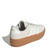 Championes Adidas modelo VL Court Bold con diseño de plataforma alta. Presentan una capellada de cuero en tono gris claro con las icónicas tres tiras laterales y detalles de marca en dorado. Cuentan con suela de goma color caramelo y cierre mediante cordones.