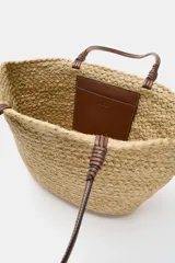 Bolso tipo shopper confeccionado en yute trenzado, con doble asa de mano en cuero sintético color marrón.