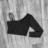 Top corto asimétrico de color gris oscuro, con un hombro descubierto, manga larga y tirantes finos en el hombro opuesto.