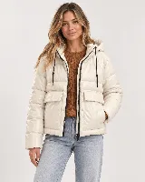 Campera puffer acolchada color beige, de diseño liviano, con capucha, cierre frontal con cremallera negra, cordones ajustables y bolsillos delanteros con solapa.