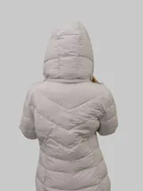 Campera puffer color beige con cierre frontal y bolsillos laterales con cierre. Tiene capucha desmontable y relleno acolchado.