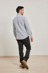 Camisa de manga larga confeccionada en tejido de algodón Oxford, con diseño de rayas verticales en tonos gris y blanco, cuello abotonado y bolsillo frontal.