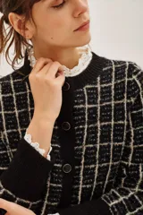 Cardigan de punto en color negro con diseño de cuadros en color beige. Presenta cuello redondo, cierre frontal con botones metálicos y mangas largas con puños anchos en color negro liso.