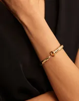 Pulsera rígida abierta bañada en oro, con diseño que simula un clavo, terminando en punta en un extremo y en forma de cabeza de clavo redonda en el otro.