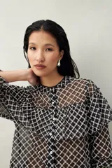 Camisa de encaje bordado semitransparente en color negro con diseño geométrico blanco. Posee silueta fluida, mangas largas, cuello mao y detalles de volados en el frente y hombros.