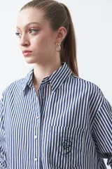 Camisa a rayas verticales blancas y marrones, de manga larga con puños abotonados, cuello camisero y botones frontales. Incluye un bolsillo en el pecho con bordado sutil.