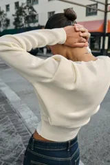Jersey de punto de cuello redondo y manga larga, con diseño estructurado que incorpora hombreras marcadas y detalles de pliegues en los hombros.