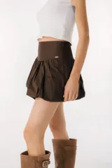 Falda corta tipo balloon color blanco, con cintura alta y diseño con volumen. Presenta una pequeña placa metálica con el logo de la marca en la parte frontal.