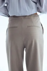 Pantalón de vestir color gris topo, tiro alto, con piernas bootcut y raya marcada en el frente y el reverso. Presenta cierre frontal con botón oculto y corchetes, bolsillos al bies y bolsillos traseros ribeteados.