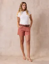 Short de jean azul oscuro con tiro medio, cierre frontal con botón y pasadores para cinturón. Incluye un cinturón trenzado de cuero sintético color marrón con hebilla circular metálica.