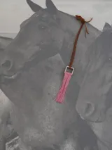 Collar con cordón de cuero tostado y dije geométrico metálico de sección cuadrada con flecos colgantes de hilo rojo.