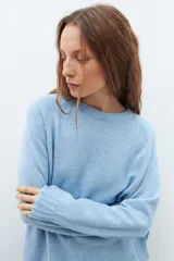 Sweater de punto en color celeste, con cuello redondo, mangas largas y puños acanalados. Presenta un diseño de corte holgado con costuras verticales decorativas en el frente.
