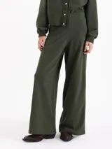 Pantalón de corte recto y silueta holgada, confeccionado en tejido rústico de algodón color verde militar. Presenta cintura con elástico interno y detalles de broches metálicos a presión en los laterales.