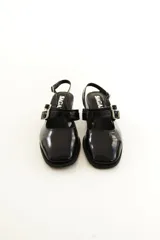 Zapatos tipo Mary Jane de charol color negro, con taco bloque, talón descubierto y doble tira frontal con hebillas metálicas.