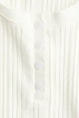 Top de manga larga en punto acanalado de algodón con diseño pointelle, escote en U con ribete festoneado y tapeta con botones al frente.